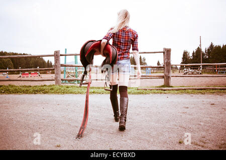 La donna caucasica portando la sella del cavallo sul ranch Foto Stock