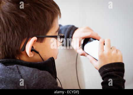 Razza mista boy ascoltando gli auricolari e utilizzando il telefono cellulare Foto Stock