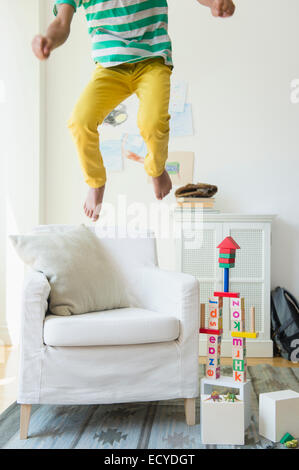 Razza mista boy salto sulla poltrona in salotto Foto Stock