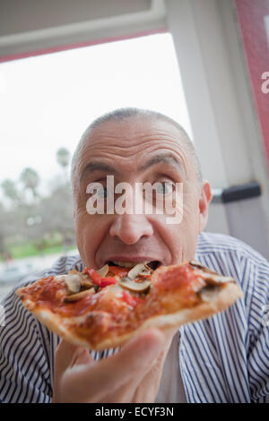 Ispanico uomo senior di mangiare un trancio di pizza Foto Stock