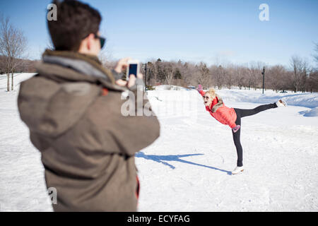 Uomo caucasico di scattare la foto della ragazza pattinaggio sul lago ghiacciato Foto Stock