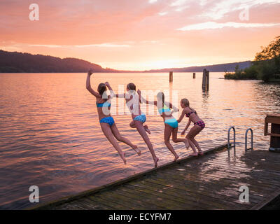 Le ragazze del salto nel lago dal dock in legno Foto Stock