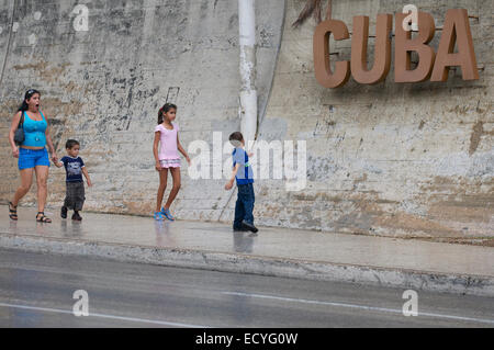 L'Avana, Cuba - Giugno 12, 2011: i giovani cubani a piedi sul marciapiede dominato dal segno di Cuba a La rampa del quartiere. Foto Stock