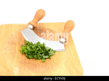 Foglie di basilico fresco tritate con un coltello oscillante su un tagliere di legno, isolato su sfondo bianco Foto Stock