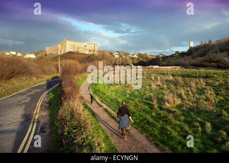 Un dog walker in Manorbier con il castello e la chiesa di San Giacomo (a destra) South Wales UK Foto Stock