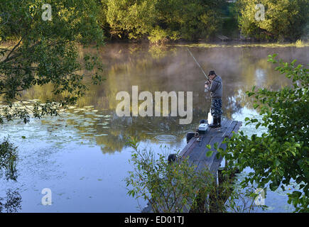 La pesca sulle rive di un fiume dal Ponte di mattina presto Foto Stock
