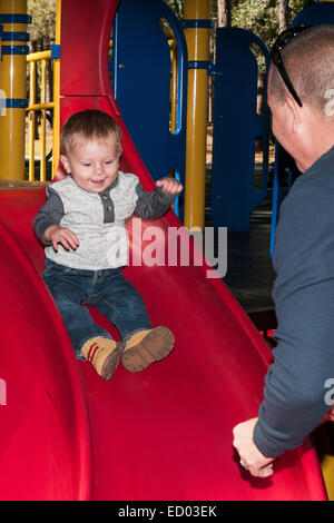 Bambino che va in giù una diapositiva rosso con Padre pronto per la cattura di lui. Foto Stock