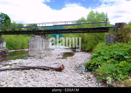 Il vecchio ponte di ferro sul fiume su uno sfondo di colline boscose Foto Stock