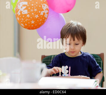 Ragazzo seduto a un tavolo dopo aver soffiato le sue candele di compleanno Foto Stock