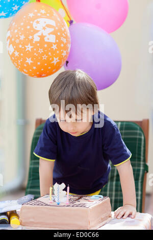 Ragazzo soffiando le candeline sulla sua torta di compleanno Foto Stock