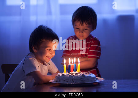 Ragazzo che sta per soffiare le candele sulla sua torta di compleanno con suo fratello che gli sta accanto Foto Stock