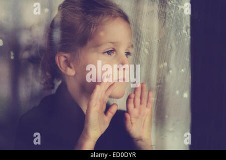 Triste ragazza che guarda attraverso una finestra Foto Stock