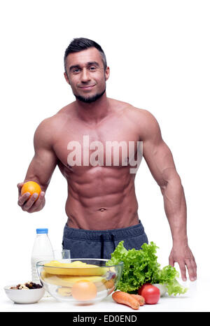 Sorridente muscolare di uomo in piedi con cibo vegetariano Foto Stock