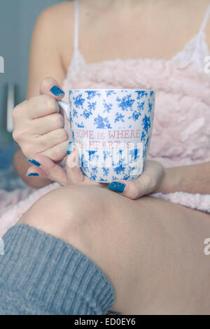 Donna seduta sul suo letto con una tazza di caffè Foto Stock