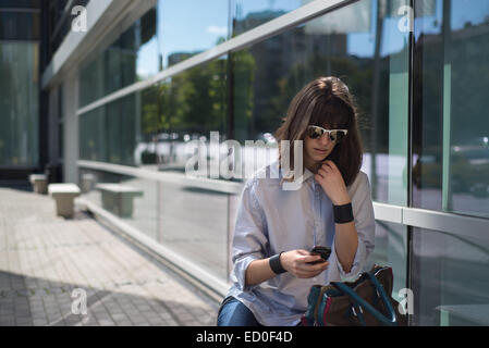 Donna seduta in strada guardando al telefono cellulare, Sofia, Bulgaria Foto Stock