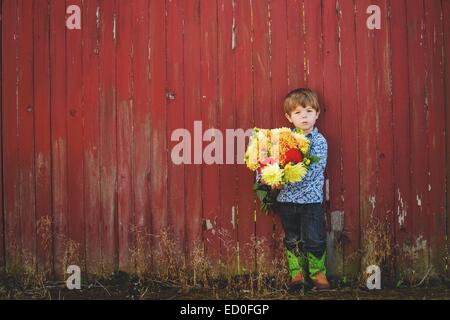 Ragazzo in piedi davanti ad una parete rossa che tiene un mazzo di fiori Foto Stock