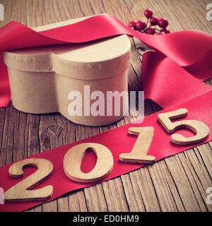 Numeri in legno formando 2015, come l'anno nuovo, un cuore a forma di scatola regalo di rosso e un nastro di raso su una tavola in legno rustico Foto Stock