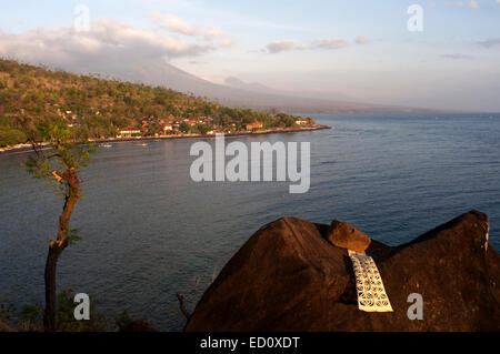 Una preghiera su di una roccia che si affaccia il piccolo villaggio di pescatori di Amed, con Gunung Agung mountain sullo sfondo (3142m). A est di Bali. Amed Foto Stock