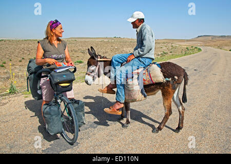 Ciclista femmina sul touring bike chiedendo indicazioni per un uomo turco su Donkey nella Turchia occidentale Foto Stock