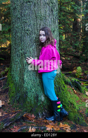 Ragazza giovane in una foresta pluviale temperata abbracciando un abete Foto Stock