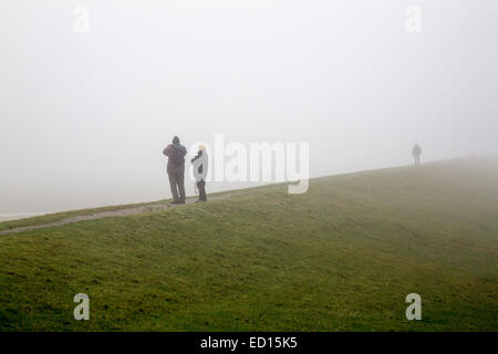 Persone su una protezione del litorale dike, in inverno, nebbia, isola del Mare del Nord Spiekeroog, Bassa Sassonia, Germania, Europa Foto Stock