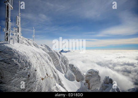 Paesaggio orizzontale di un grigio, incolore alpina con la cima ricoperta di brina antenne radio circondato da nubi. Foto Stock
