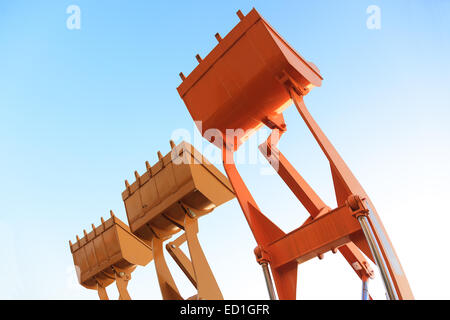 Parte del moderno di colore giallo macchine escavatore,le benne/pale sollevate contro il cielo blu in un sito in costruzione. Foto Stock