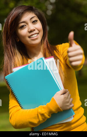 Collegio femminile studente con libri gesticolando pollice in alto in posizione di parcheggio Foto Stock