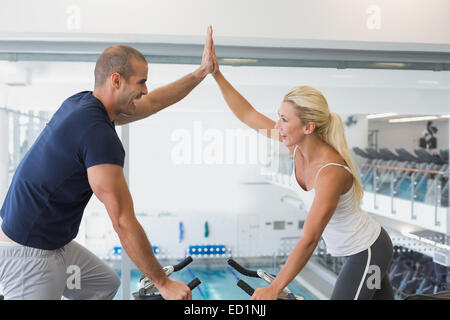 Montare il giovane dando alta cinque mentre si lavora su una cyclette in palestra Foto Stock