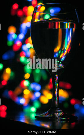 Bicchiere di vino al buio durante una celebrazione come il Natale o il nuovo anno con albero di Natale luci in background. Foto Stock