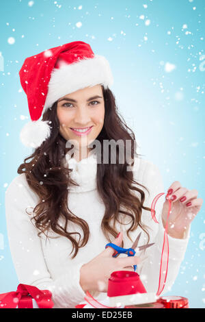 Immagine composita di sorridere brunette in santa hat doni di imballaggio Foto Stock