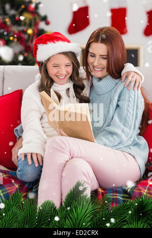 Immagine composita di festosa madre e figlia la lettura sul lettino Foto Stock