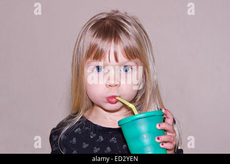 Una giovane ragazza caucasica bere latte da una cannuccia isolata contro uno sfondo neutro. Foto Stock