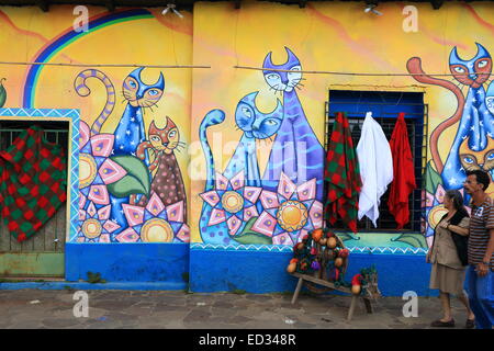 Due persone locali oltrepassando un vivacemente colorato murale dipinto sulle pareti di una strada in Ataco, Ahuachapán, El Salvador. Foto Stock