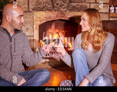 Felice coppia giovane seduto vicino al camino e bere il vino, romantiche data, celebra il giorno di San Valentino Foto Stock