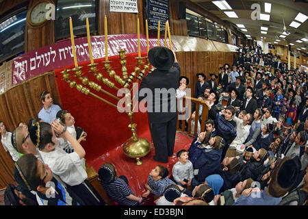 Un ortodosso rabbino ebreo luci Hanukkah candele come studenti e congregants guardare in una sinagoga di Brooklyn, NY Foto Stock