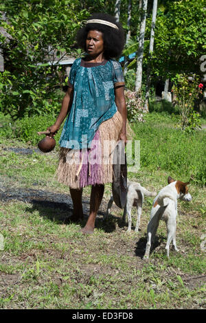 La Melanesia, Papua Nuova Guinea, Dobu isola. Donna in erba gonna con piastra in legno circondato da cani. Foto Stock