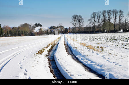 Inverno inglese paesaggio rurale con la via attraverso una coperta di neve campo e Borgo Foto Stock