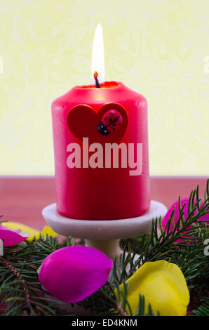 Red christmas candle burning, decorata da un ramo di abete e petali di rosa Foto Stock