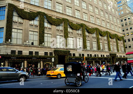 La città di New York: un pedicab taxi passa il leggendario Saks Fifth Avenue department store adornata con decorazioni di Natale Foto Stock