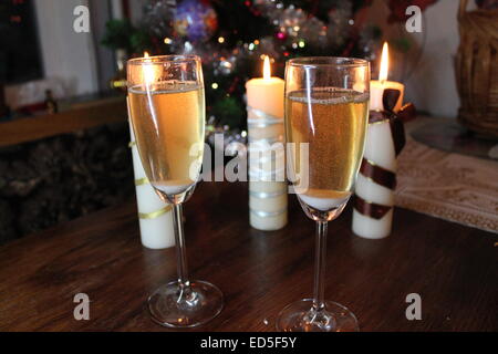 Due bicchieri di cristallo pieno di golden champagne e tre candele accese preparazione per la celebrazione del Natale praticamente Foto Stock