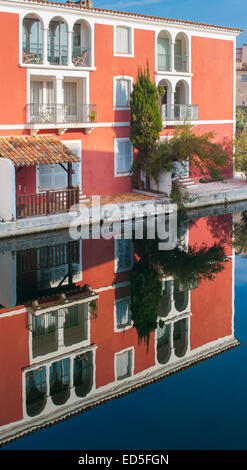 Un piccolo rosso tipico edificio di Port Grimaud, nel sud della Francia, si riflette nelle calme acque di un canale Foto Stock