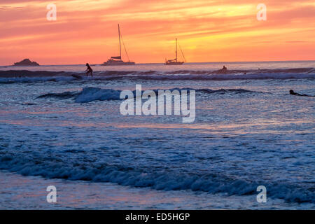 Surfers stagliano contro il sole di setting su Playa Tamarindo, Guanacaste in Costa Rica Foto Stock