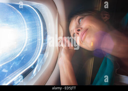 Felice, femmina passeggero aereo godendo la vista dalla finestra della cabina sopra il cielo blu (SHALLOW DOF; flare intenzionale) Foto Stock