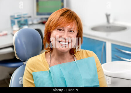 Sorridente donna senior con nuovi impianti dentali seduto in studio dentistico Foto Stock