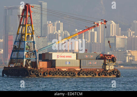 A pieno carico Derrick Barge caricato con i contenitori di spedizione, sotto il traino in porto di Victoria e di Hong Kong. Foto Stock