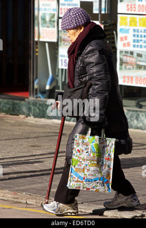 Anziani donna cinese attraversando la strada a Hong Kong durante l'inverno. Foto Stock