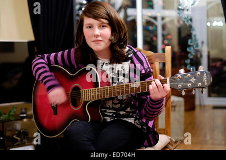 Ragazza di dodici anni a suonare la chitarra per la sua famiglia per Natale Foto Stock