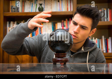 Giovane uomo predire il futuro guardando nella sfera di cristallo Foto Stock