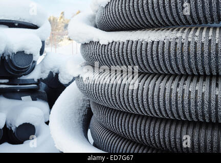 Rotoli di tubi in materia plastica o tubi impilate in cortile, la presenza di neve e freddo giorno Foto Stock